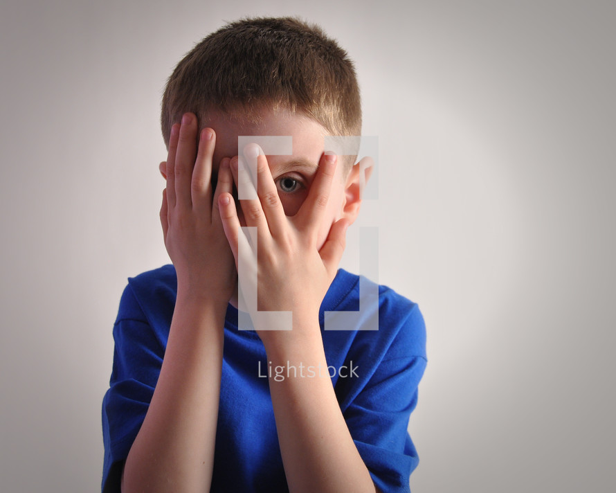 a boy covering his face and peeking through his fingers 