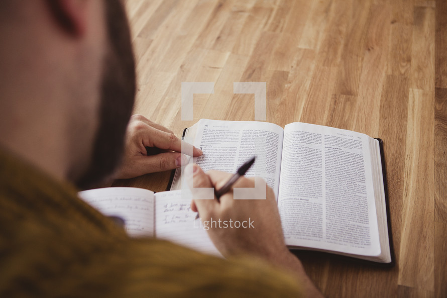 man reading a Bible and writing a journal
