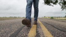 feet of a man walking on the center lines of a road 
