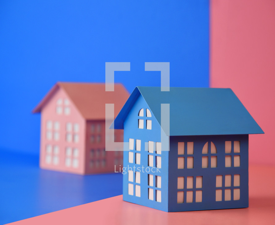 A blue house and a pink house are side by side against colored backgrounds for a gender opposite conceptual message.