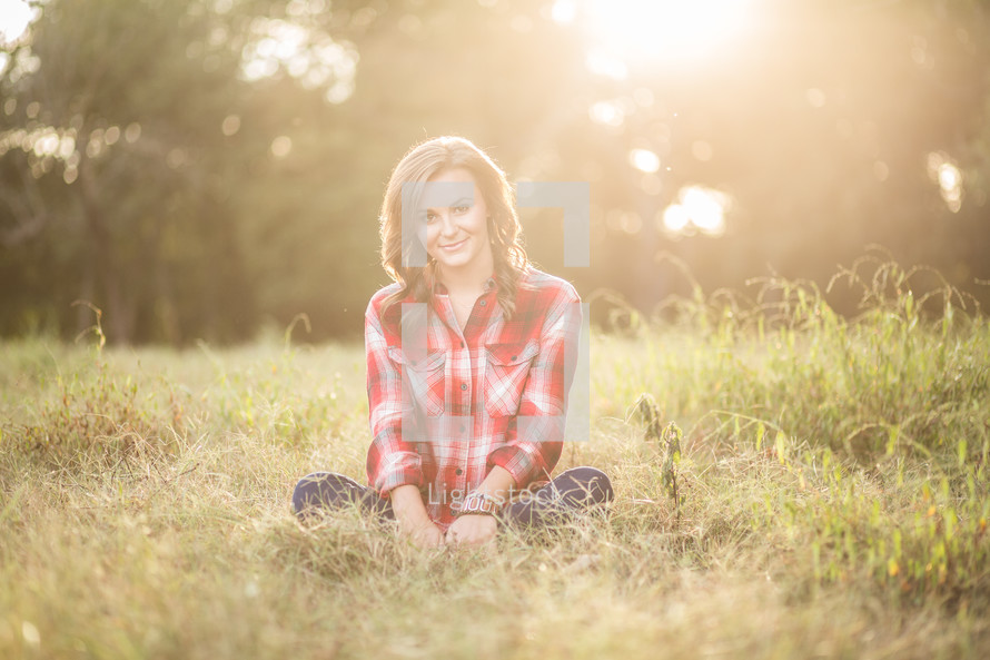 a woman sitting in grass wearing a plaid shirt 