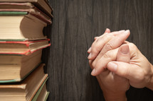 Hands in prayer by vintage books on a dark wood table