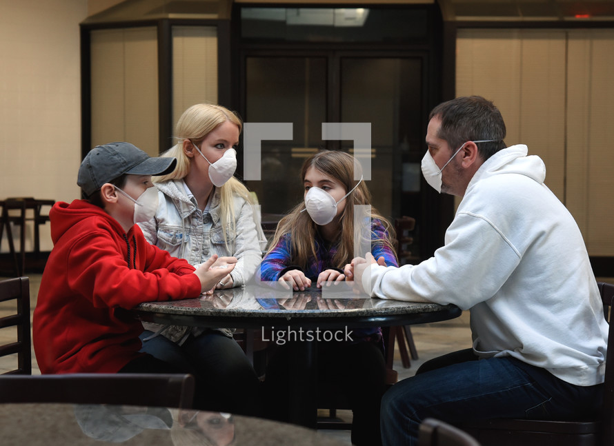 A family is sitting together at a table together wearing a protective face mask for a virus or health concept.
