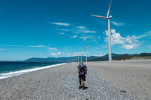 wind turbines along a shore and man walking on beach 