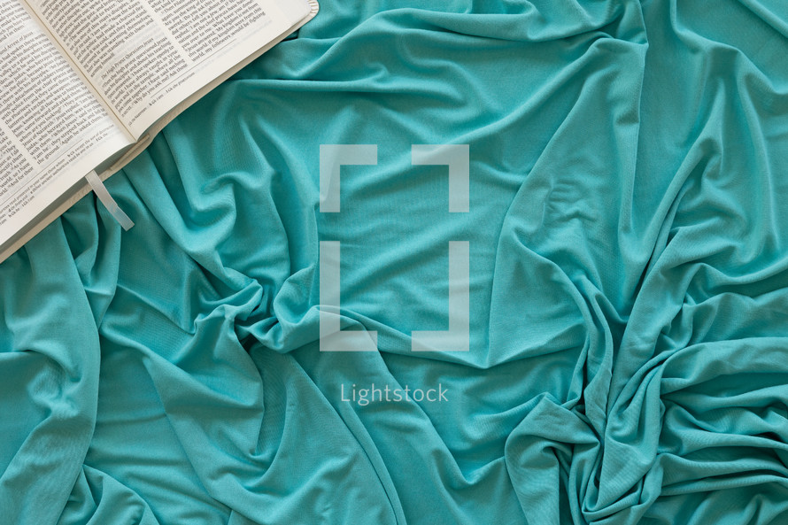 Open bible on a teal blanket background with copy space