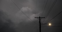 Dramatic lightning in dark, moody thunderstorm clouds behind of electrical wire.