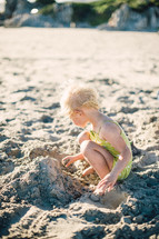 toddler girl in a bathing suit playing in the sand 