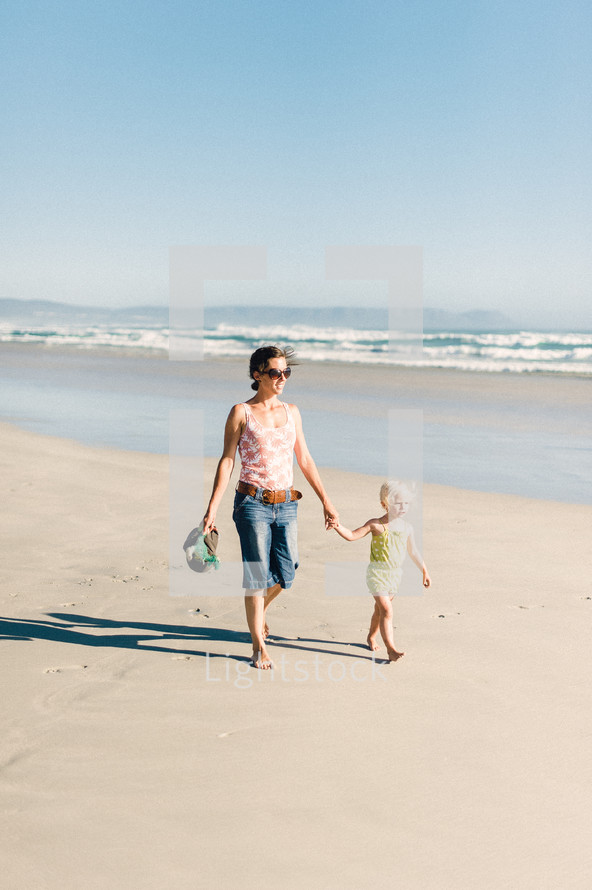 mother and daughter walking holding hands on beach 