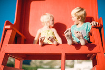 siblings sitting in a lifeguard stand on a beach 