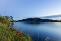 A placid lake with hills and a tower in the distance.