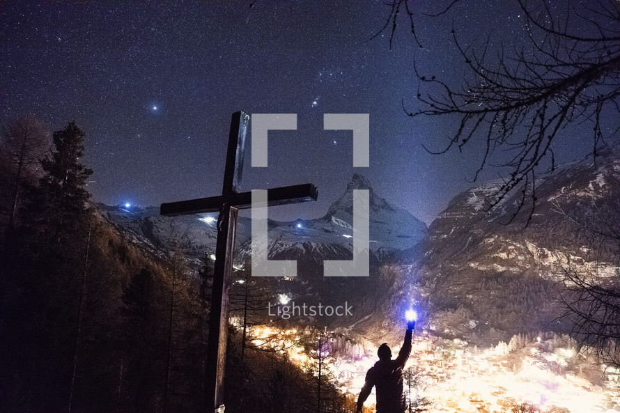 cross and man shining a flashlight and mountains 