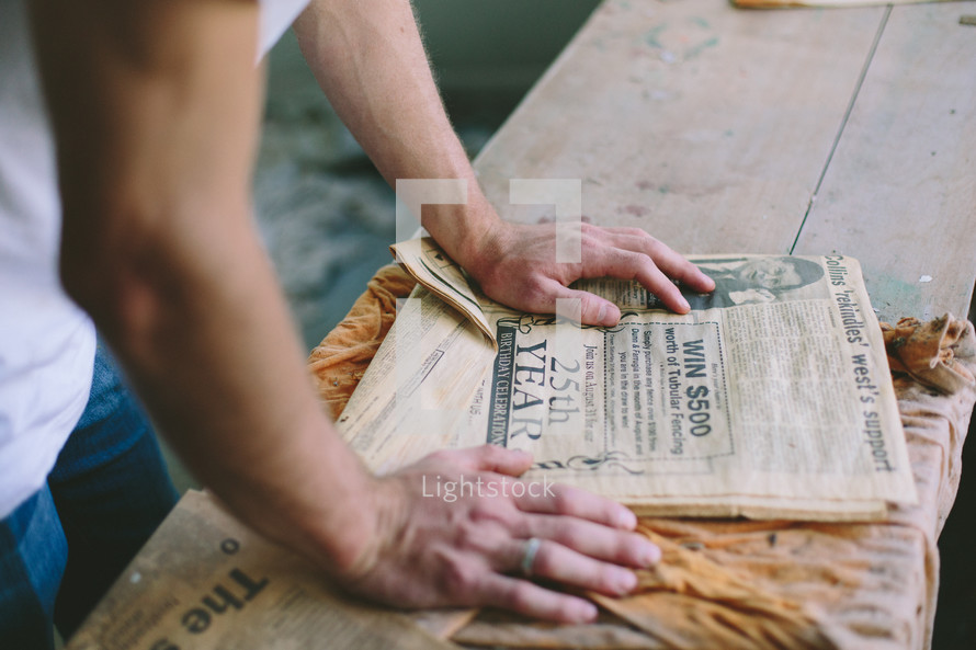Hands on a newspaper on a wooden table.