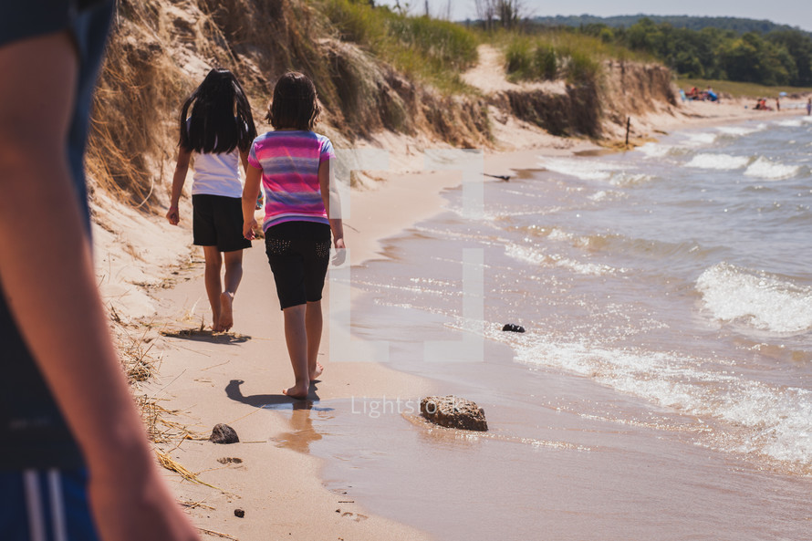 Two young girls walking along a beach.