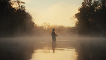 Young fly fisherman casting on a foggy river at sunrise