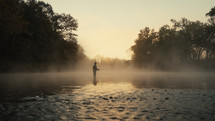 Young fly fisherman casting on a foggy river at sunrise