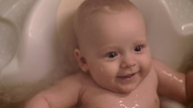 Slow motion close-up shot of happy baby bathing. Cheerful child of five months old in water