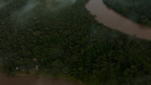 Drone tilt up shot of green forest landscape with Amazon River during cloudy day.