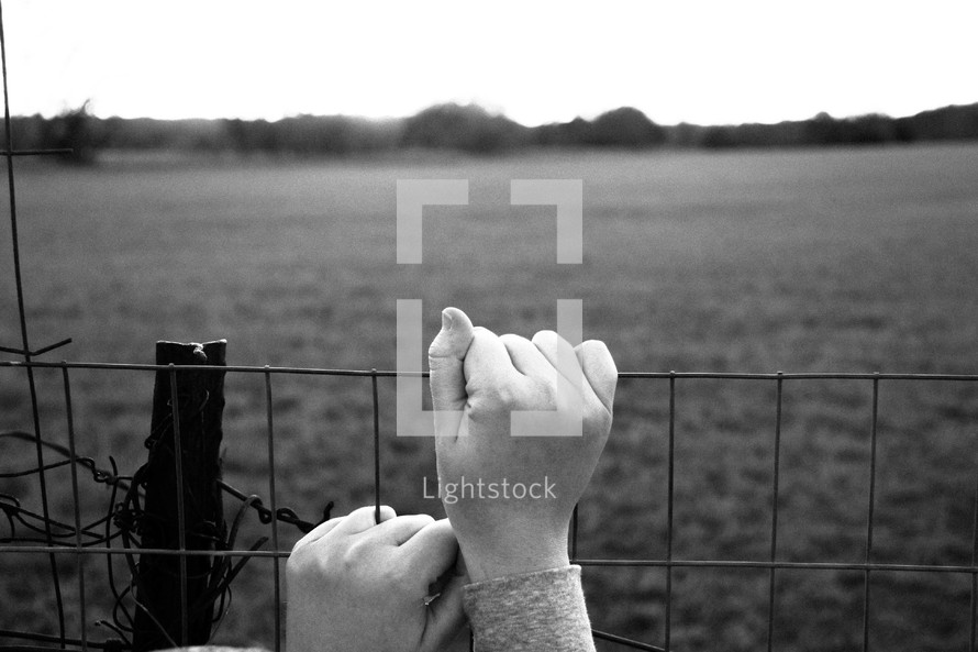 Hands clinging to a fence.