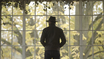 man in a hat looking out a window 