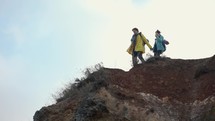 The active man and woman walking on rocks with backpacks.