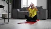 Serious young man meditating at home moving hands in namaste on yoga mat.