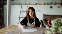 a red-haired girl draws a scheme of her product on paper with a pencil.