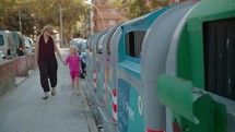 Woman and child disposing paper in recycling bin on city sidewalk