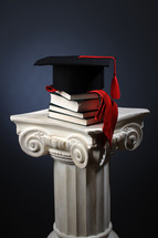 graduation cap on books on a column 