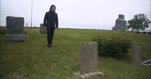 Young, sad man in black suit in cemetery at graveyard tombstone grieving in cinematic slow motion.