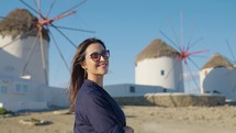 A beautiful tourist woman enjoys the view to the famous windmills on Mykonos island, Greece, during her summer holidays