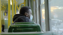 a man riding  a city bus wearing a face mask 