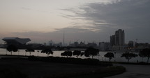 Distant Dubai skyline with Burj Khalifa and other buildings and skyscrapers in front of river in the evening.