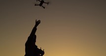 Silhouette of man pilot a drone with remote controller in the nature at sunset