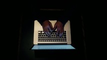 hands typing on a laptop in darkness 