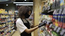 Female staff in mask working at grocery section of supermarket.