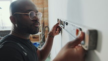 African American man using spirit level and examining surface of the wall when doing DIY home renovation
