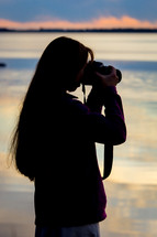 a woman taking a picture at sunset 