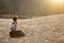 a woman sitting in a field praying 