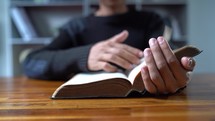 Close up hands of man reading Bible at wooden table in morning, Christian concept.