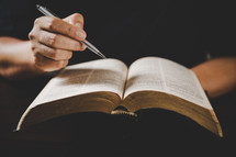 Person holding a pen and a Bible