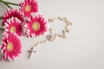 Pink flowers and a white rosary on a white background
