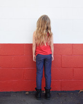 A child is standing in front of a brick red wall outside for a challenge or obstacle concept