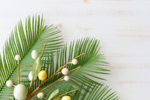 Easter eggs, palm fronds, and crown of thorns on a white wood background 