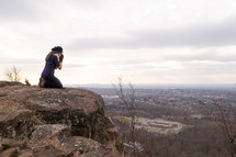a woman kneeling in prayer on a mountaintop 
