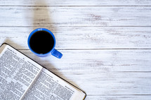open Bible and coffee mug on a white wood background 
