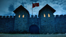 Roman military fort with illuminated windows and the flag fluttering at night.
