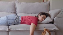 Exhausted or bored young sleepy woman falls down on sofa. Lovely dog tries to cheer her up.
