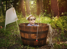 a boy sitting in a barrel holding a fishing pole in a forest 