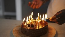 Man's hand lighting candles on birhday cake in a dusk, close up.