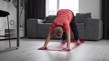 Old woman exercising legs laying on yoga mat in living room.